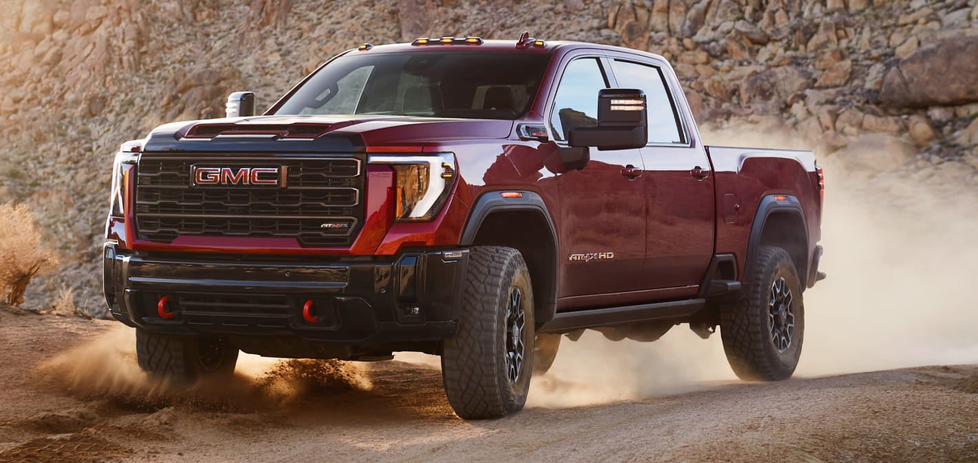 2026 GMC Sierra 2500 HD drives on a rocky terrain and showcasing its rugged design and power.