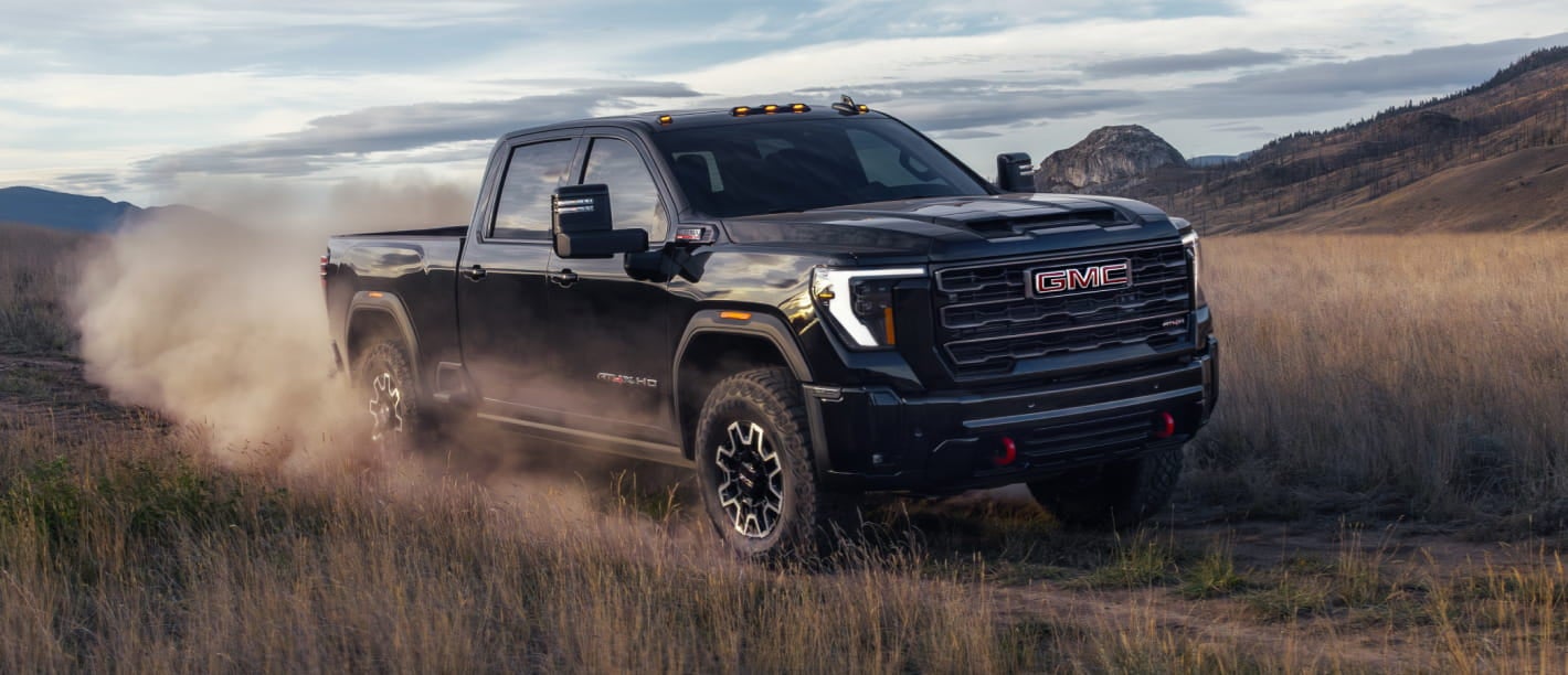 2026 GMC Sierra 2500 HD truck drives off-road through a grassy field.